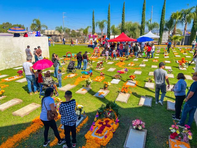 Familias visitan las tumbas decoradas con cempasúchil en los jardines del cementerio