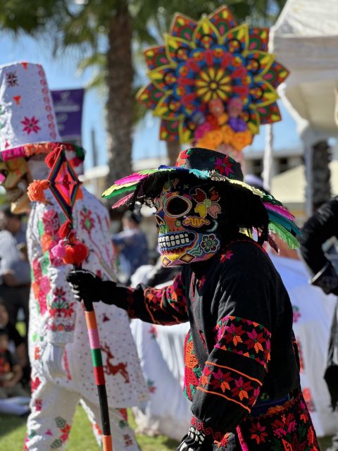 Danzante de Xantolo con máscara de calavera pintada, sombrero de plumas y traje negro bordado de flores