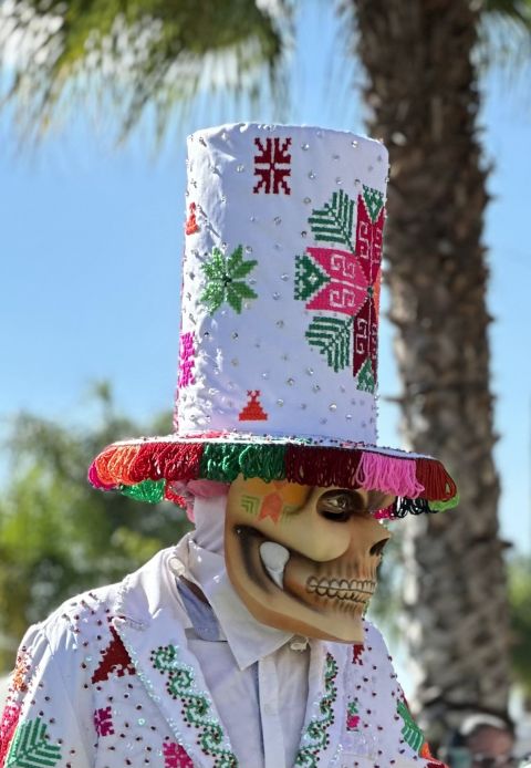 Danzante de Xantolo con máscara de calavera, traje blanco bordado y un alto sombrero de copa blanco con bordados de colores