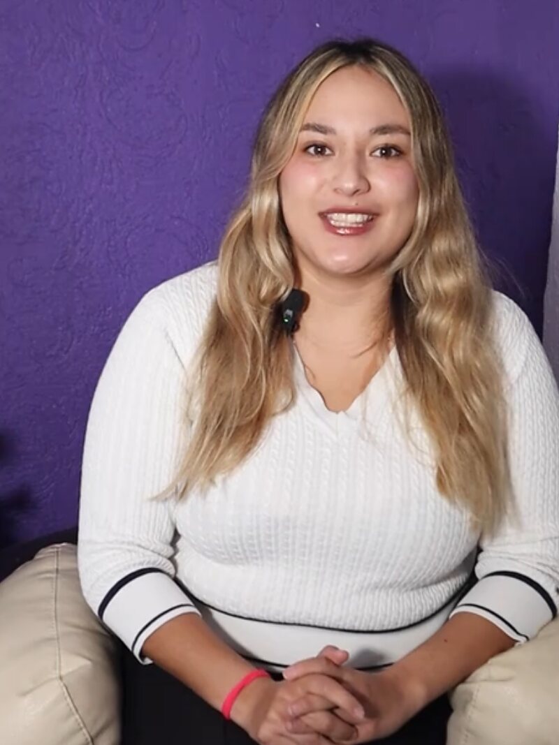 La tanatóloga de Jardines Perpetuos, sentada frente a una pared morada durante la grabación de uno de sus videos